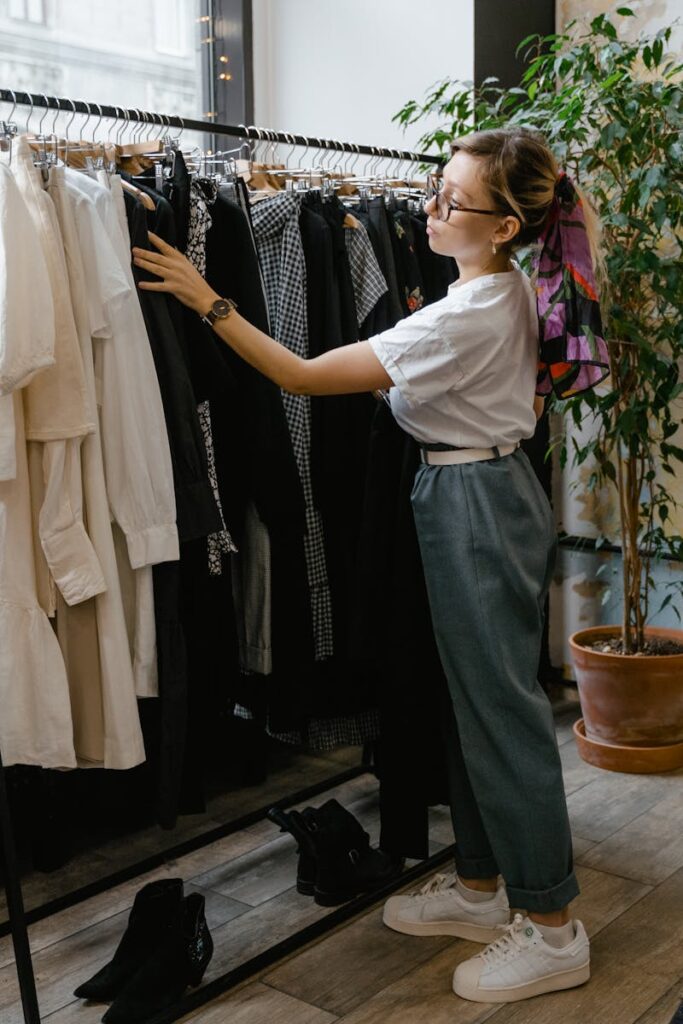 A stylish woman browsing clothes in a chic boutique store with ceramics and plants.